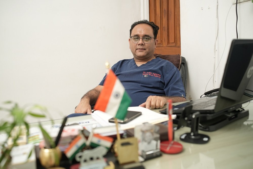 Dr. Ankit Agrawal, cardiologist, sitting at his office desk with laptop and Indian flag at Infinity Heart Institute Jabalpur