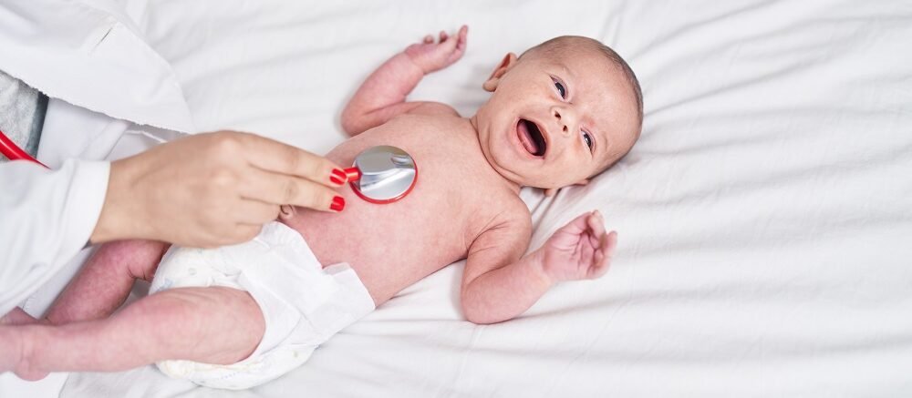 "Doctor using stethoscope to examine newborn baby lying on white bed"