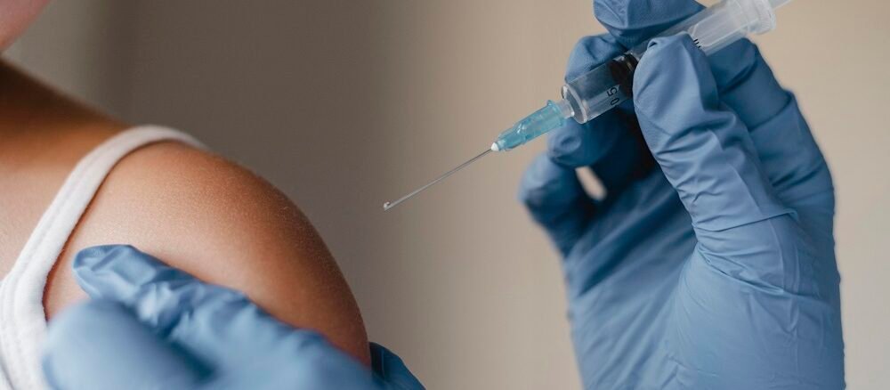 "Doctor with blue gloves holding syringe, about to give injection in patient’s upper arm"