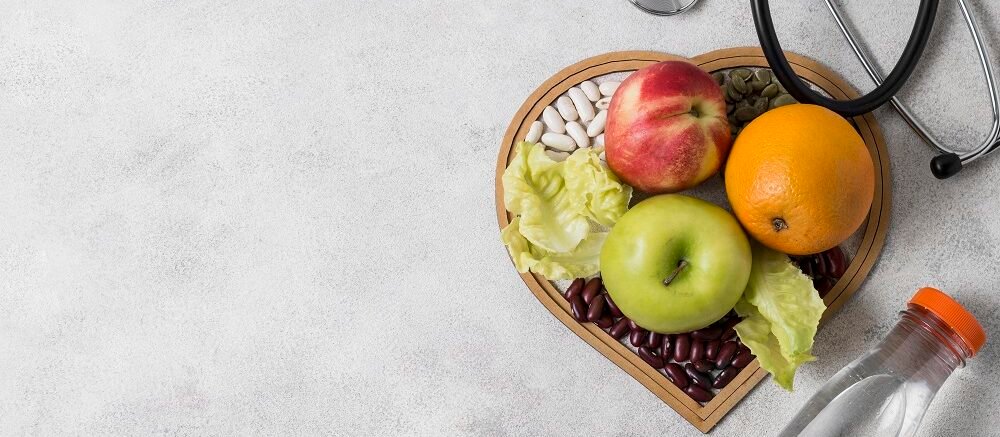 "Heart-shaped bowl with fruits, seeds, beans, lettuce, bottle of water, and stethoscope, showing heart healthy diet"