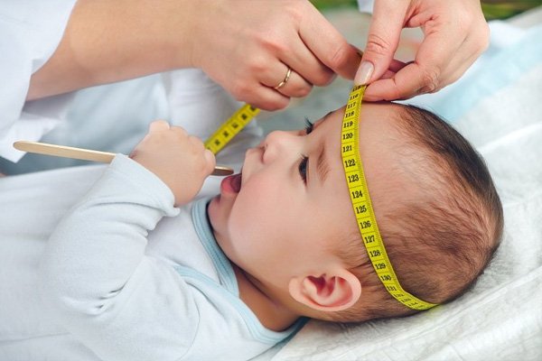 "Doctor measuring baby head circumference with measuring tape during pediatric checkup"