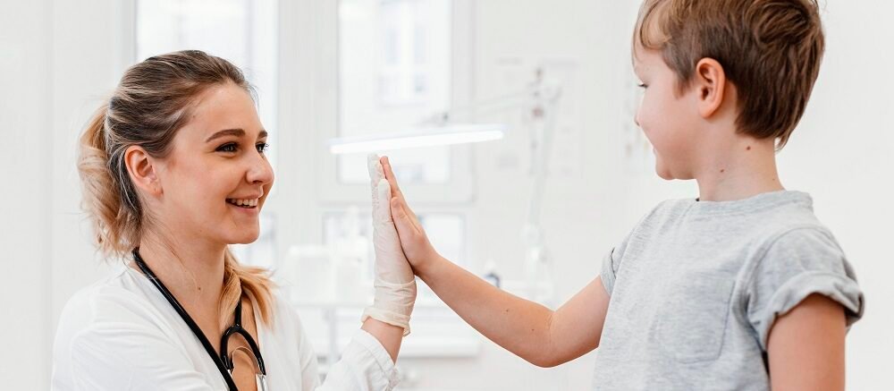 "Smiling female doctor high-fiving happy young boy during clinic visit"